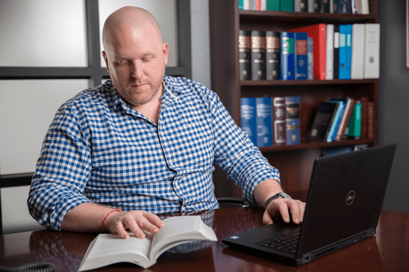 A lawyer sits at his desk referencing a book and working on a computer.