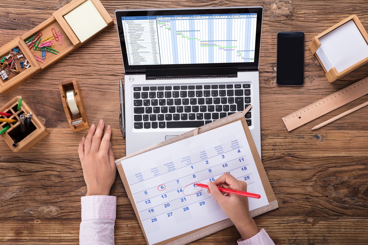 Someone circling a date on a calendar with a laptop in the background