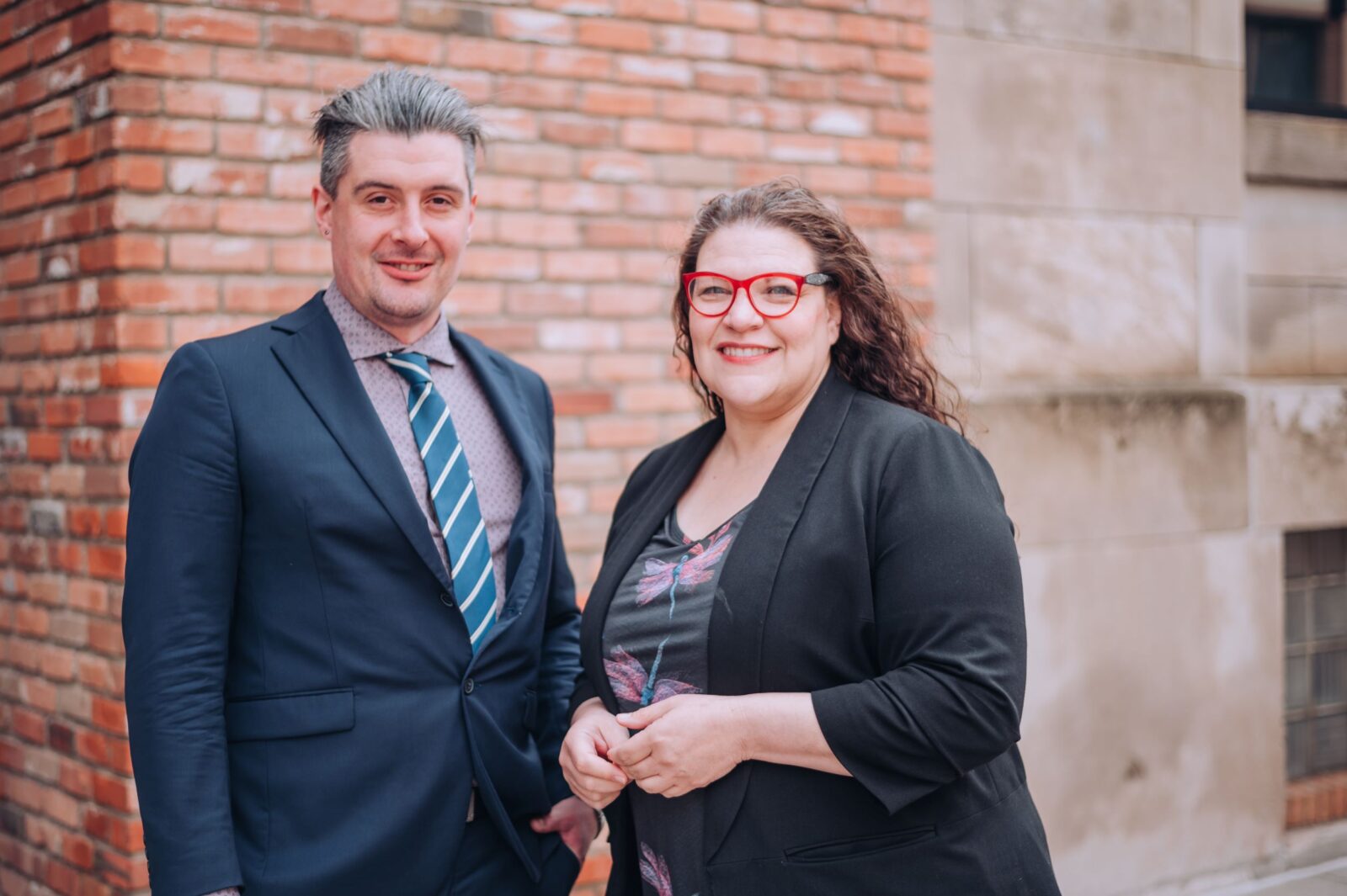 Male and female lawyer standing in front of a brick building smiling at the camera