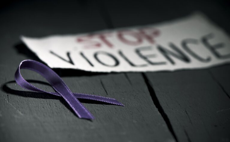 a purple ribbon for the awareness about the unacceptability of the violence against women and the text stop violence on a piece of paper, on a dark gray rustic wooden surface