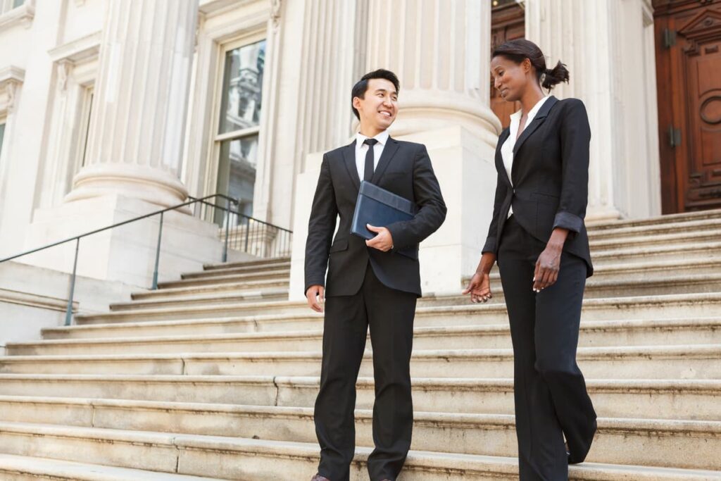 two lawyers wearing suits standing on the steps of a courthouse having a conversation