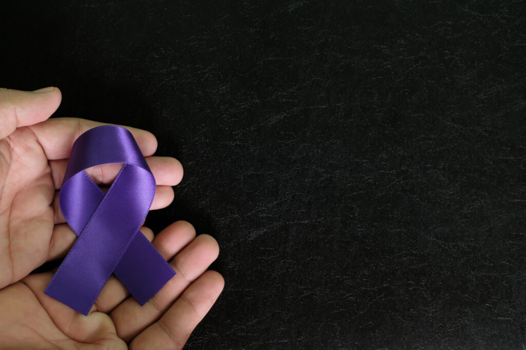 Human hand holding purple ribbon color on dark black background for Family Violence Prevention Month